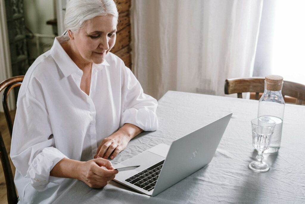 Elderly woman using laptop for online shopping at home during daytime.