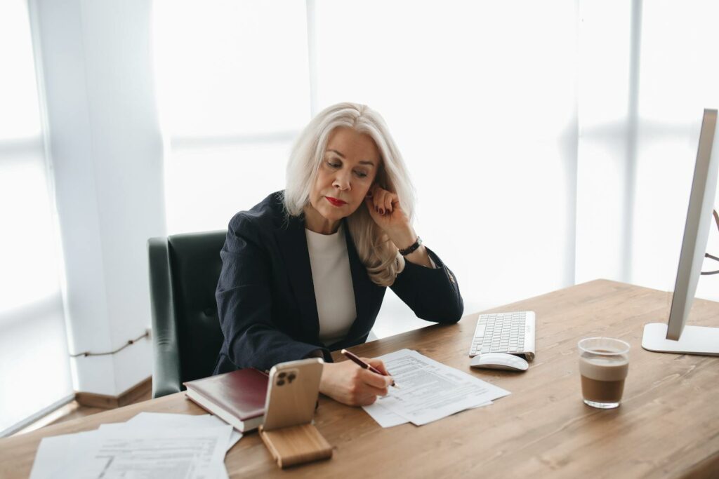 Woman reviewing documents at a desk with a smartphone and computer in a modern office.